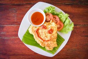 Rollo de tortilla con ensalada de tomates en rodajas lechuga vegetal en un plato blanco - desayuno de tortilla de huevos y salsa de tomate en la parte superior foto