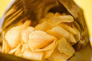 las papas fritas son un bocadillo en un paquete de bolsas envuelto en plástico listo para comer y comida grasa o comida chatarra, papas fritas con fondo amarillo foto