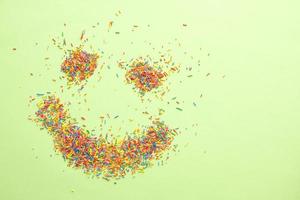 Smiling emoji made of sweet colorful sugar sprinkles on green background with free copy space. photo