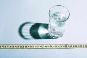 adietando un concepto de pérdida de peso bodegón. vaso de agua y una cinta métrica. foto