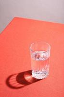 Glass of water with hard shadow on a table with red cloth. photo