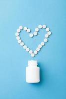 Simple medicine and healthcare concept flat lay. White plastic bottle and heart shaped layout made of pills. photo
