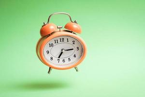 Orange vintage style flying alarm clock. Flying alarm clock on green background. photo