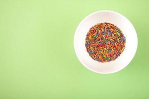 Colorful sugar sprinkles on a white pot on green background. photo