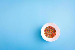 White pbowl with colorful sugar sprinkles on blue background with free copy paste space. photo