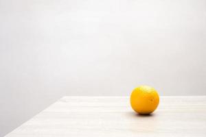 Minimalist still life image with a single orange on a table. photo