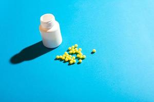 Round yellow ball pills and a plastic bottle on blue background. photo