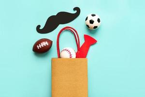 Happy Father's Day. Top view of shopping bag with false mustache,false bow tie and sports balls with space for text. Father's Day celebration concept photo