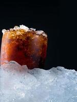 Soft drink with crushed ice cubes in glass put on pile of ice cubes on dark background with copy space. There is a drop of water on the transparent glass surface. photo