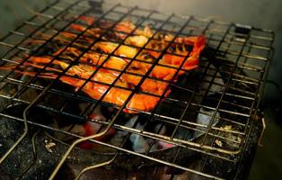 Grilled prawn on charcoal grill. Giant freshwater prawns grill on a flaming charcoal fire. Closeup giant river prawn cooking on barbecue grill rack. Cooking food for the party. Thai food culture. photo