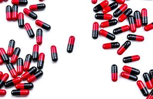 Red-black capsule pills spread on white background. Antibiotic drug use with reasonable. Pharmaceutical industry. Pharmacy background. Global healthcare. Pile of pills with unique pattern texture. photo