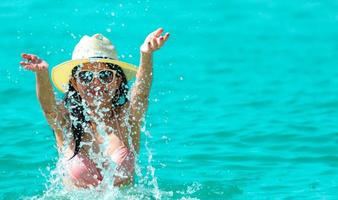 una joven asiática feliz con traje de baño rosa se relaja y disfruta de unas vacaciones en la playa del paraíso tropical. chica en vacaciones de verano salpica agua en el mar. modelo sexy mujer sexy en bikini rosa viejo. vibras de verano foto