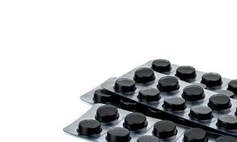 Activated charcoal tablets pills in blister pack isolated on white background with copy space for text. Black round pills for treatment poisoning from take drug overdose photo