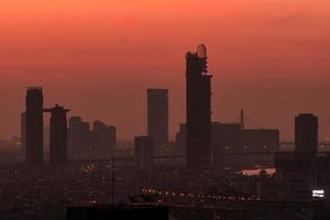 paisaje urbano por la mañana con el cielo rojo del amanecer. ciudad cubierta de smog. problema de la contaminación del aire. edificio rascacielos en el centro. horizonte urbano. silueta moderno edificio de oficinas y hoteles en la ciudad al amanecer. foto