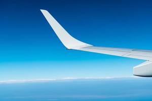 Wing of plane over white clouds. Airplane flying on blue sky. Scenic view from airplane window. Commercial airline flight. Plane wing above clouds. Flight mechanics concept. International flight. photo