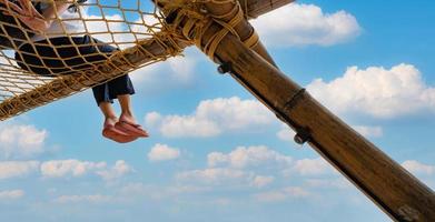 viajes de verano en la playa con cielo azul y nubes blancas. vibras de verano. vacaciones de verano. relajarse en vacaciones. mujer con flip-flop rosa sentarse en la cuerda de la red con disfrutar y relajarse en el estado de ánimo de vacaciones en el resort. foto