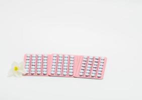 blister de hormonas para el tratamiento de mujeres menopáusicas y flor blanca sobre fondo blanco. Terapia de reemplazamiento de hormonas. pastillas redondas recubiertas de azúcar en un blister rosa. píldoras de la felicidad. menopausia. foto