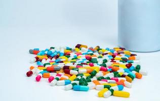 Colorful capsule pills near plastic drug bottle. Multi-colored capsule pills on white table. Pharmacy drugstore products. Pharmaceutical industry. Health budget and policy. Bright colors capsule pills photo