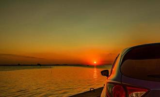 Back scene of blue compact SUV car with sport and modern design parked on concrete road by the sea at sunset. Environmentally friendly technology. Business success concept. photo