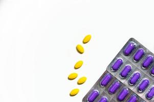 Macro shot of yellow oval tablet pills on white background and purple caplets pills in blister pack. Mild to moderate pain management. Pain killer medicine. Paracetamol and ibuprofen tablet pills. photo