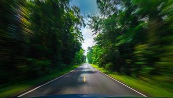 View from front of blue car on asphalt road and speed motion blur on highway in summer with green trees forest at countryside