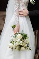 The bride in an elegant wedding dress holds a beautiful bouquet of different flowers and green leaves. Wedding theme photo