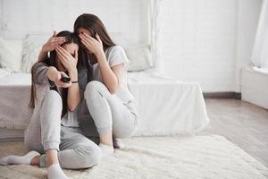 Scary moment. Sisters have fun watching TV while sits on the floor of beautiful bedroom at daytime photo