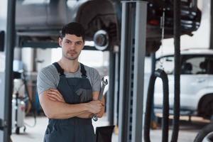 Let's get it started. Portrait of serious worker in uniform that stands in his workshop with wrench in hand photo