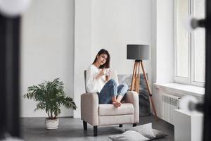 Cuarto espacioso. la joven morena se sienta en la silla cuando la luz del día entra por la ventana foto