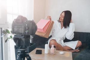 Different packages. In front of camera on the tripod. Conception of fashion and skincare. Brunette girl uses cosmetics photo