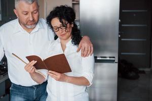 Attention needed. Man and his wife in white shirt preparing food on the kitchen using vegetables photo