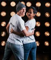 Turned to the camera. Back view of couple in shirts with their names on it standing next to studio lights photo