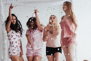 la fiesta va bien. confeti en el aire. las chicas jóvenes se divierten en la cama blanca en una bonita habitación foto