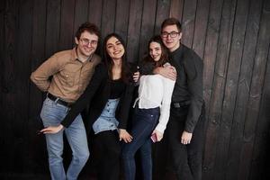 el chico abraza a la chica. el joven se para contra la pared de madera negra. grupo de amigos pasando tiempo juntos foto