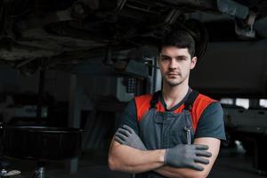 Portrait of serious worker in uniform that stands in his workshop with wrench in hand photo