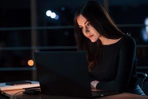 Different digital devices on the table. Attractive brunette businesswoman works alone in the office at nightime