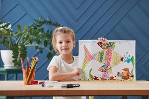 Showing off and feeling satisfaction. Cute little girl in art school shows her first paintings drawn by pencils and markers photo