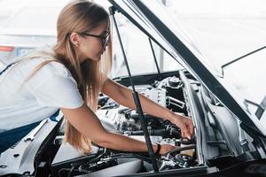 Demanded profession. On the lovely job. Car addicted woman repairs black automobile indoors photo