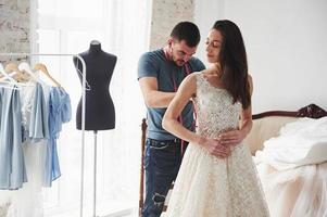 el hombre está ayudando a la novia. el proceso de ajuste del vestido en el estudio de ropa artesanal foto