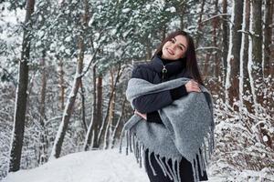 retrato de mujer encantadora en la chaqueta negra y bufanda gris en el bosque de invierno foto