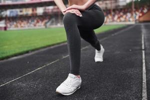 Squatting in the morning time. Young blonde warming up on the track in the stadium at daytime photo