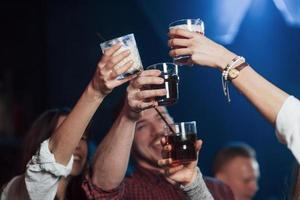 Let's drink for our happiness. Group of young friends smiling and making a toast in the nightclub photo