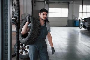 Black pipes on the left side. Mechanic holding a tire at the repair garage. Replacement of winter and summer tires photo