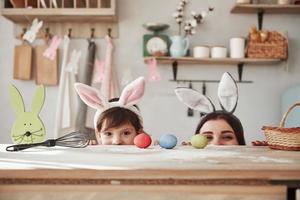 Looking fron under the table. Mother and daughter in bunny ears at easter time have some fun in the kitchen at daytime photo