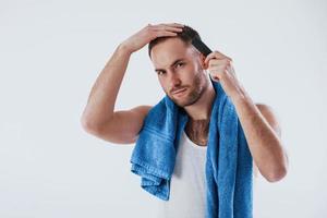 arreglar un corte de pelo elegante. el hombre con una toalla azul se alza contra un fondo blanco en el estudio foto