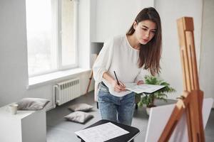 Home designer is on the work. Young brunette in the room with white walls and daylight that comes from the window photo