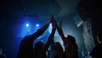 es chocar los cinco. grupo de personas que disfrutan bailando en la discoteca con hermosas luces foto