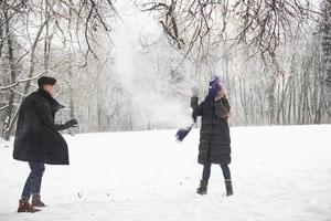 bufanda han volado. hermosa pareja joven jugando y lanzando bolas de nieve en el bosque de invierno foto