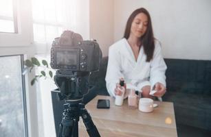 Black professional camera. In front of camera on the tripod. Conception of fashion and skincare. Brunette girl uses cosmetics photo