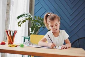 buen interior durante el día. linda niña en la escuela de arte dibuja sus primeras pinturas con lápices y marcadores foto